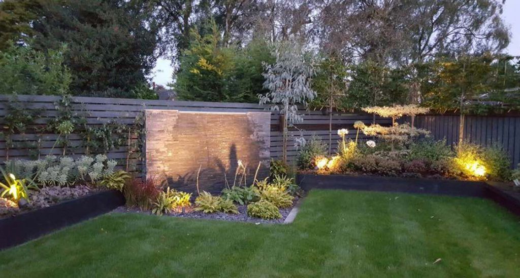 A water feature lit from below with planting beds picked out either side, so the garden still has a focal point after dark.